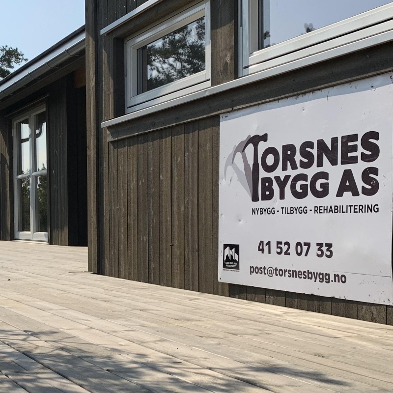 Torsnes Bygg AS sin logo på en plakat på husvegg.